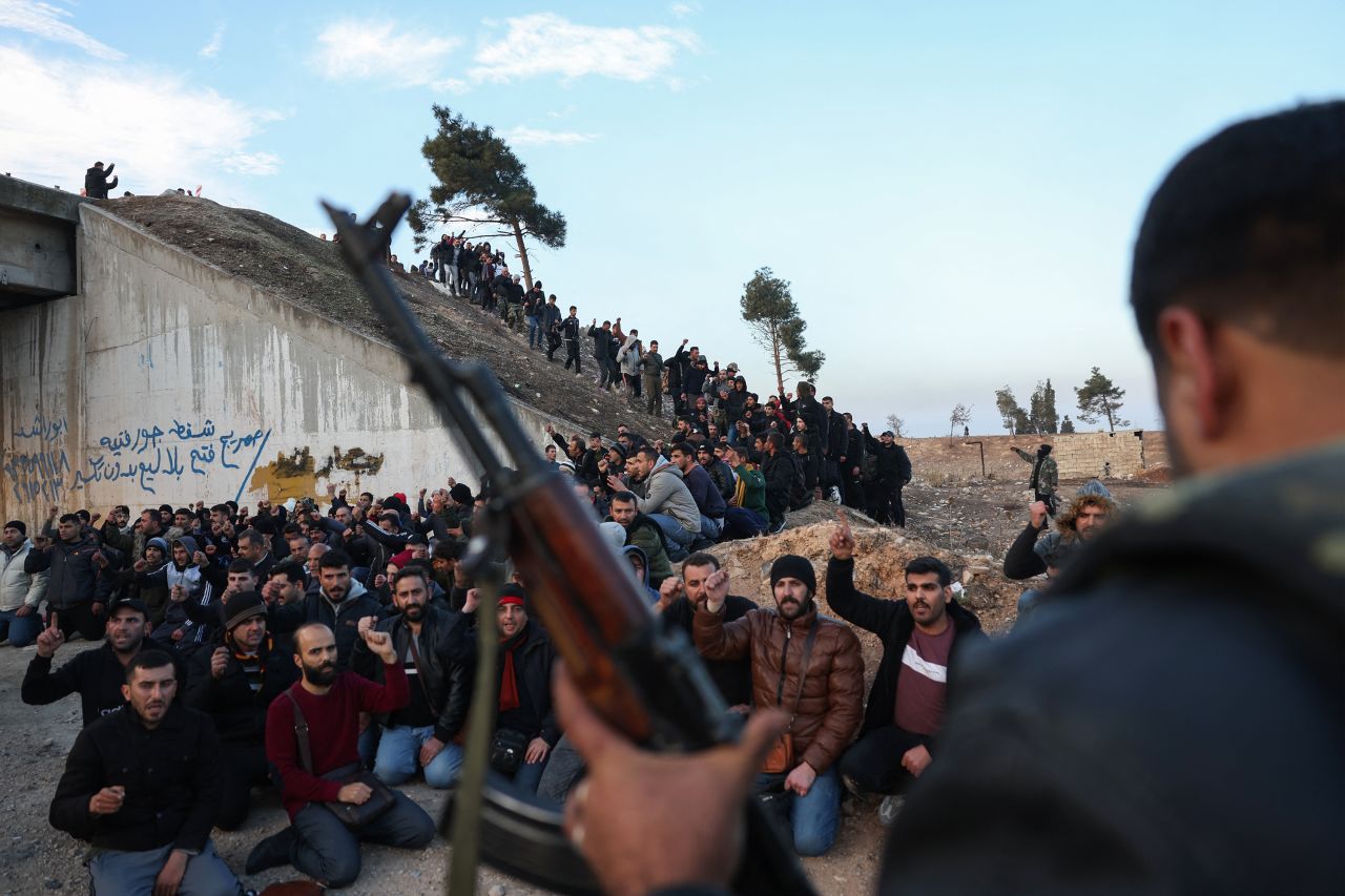 An anti-government fighter stands guard over detained pro-government soldiers outside the central city of Homs, Syria, on December 8.