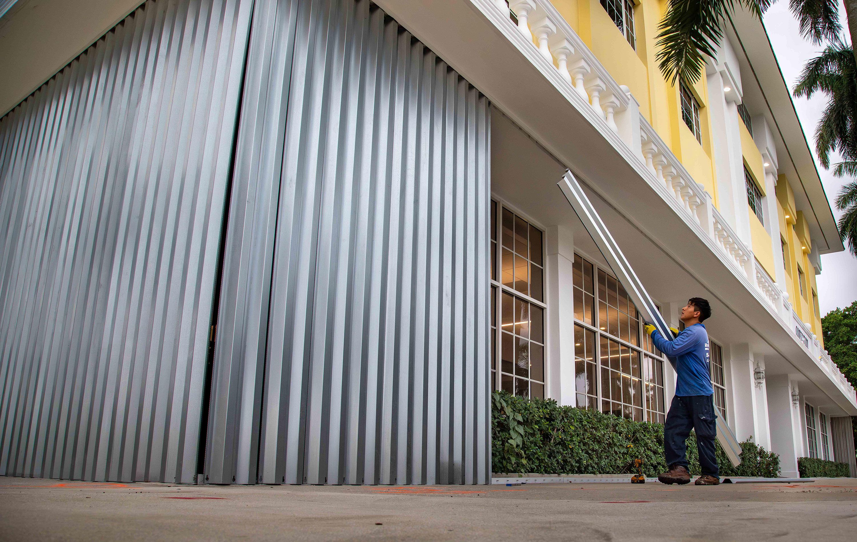 An employee of Roofs Done Right attaches metal shutters to a Palm Beach building on Wednesday.