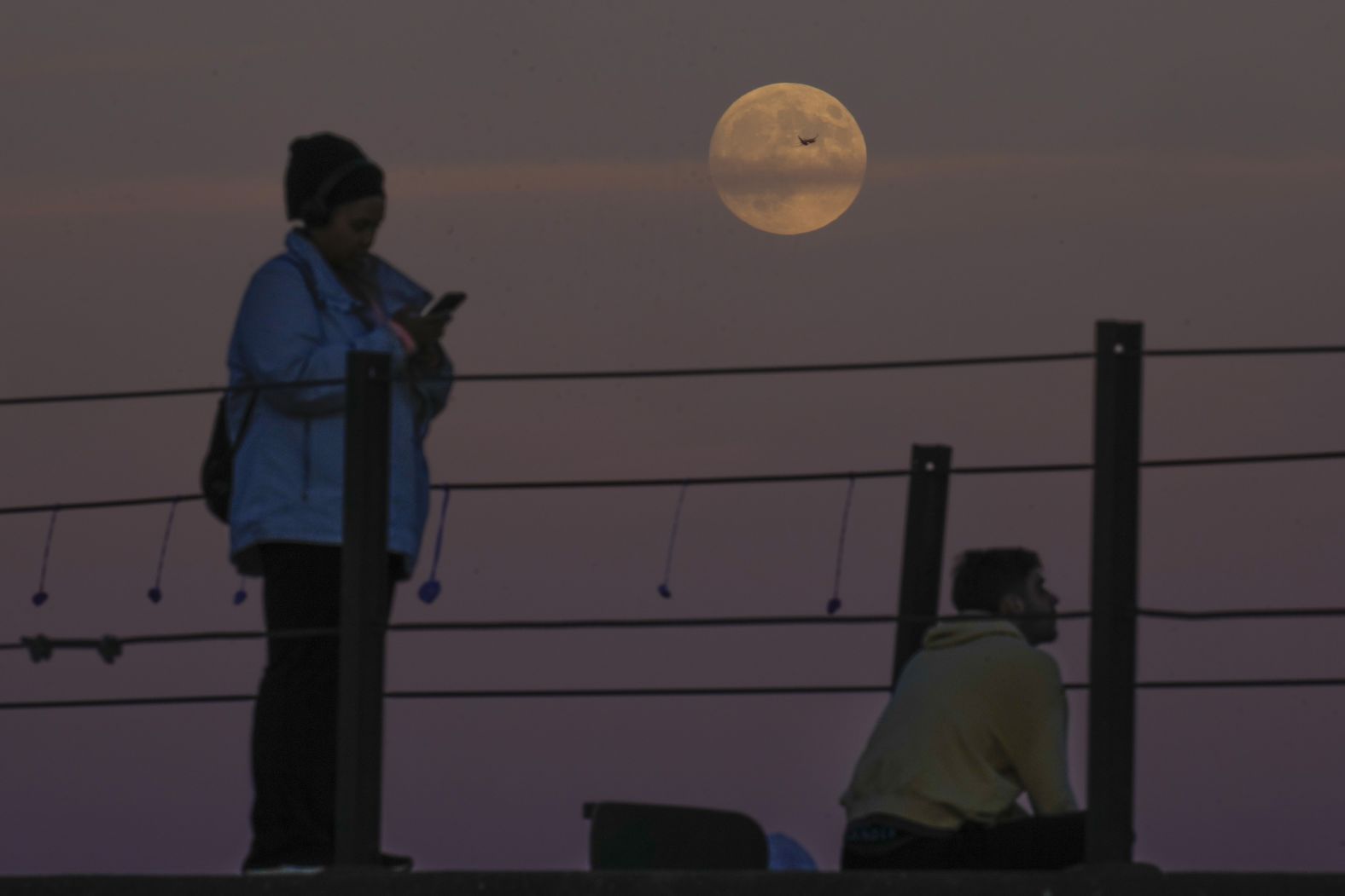 An airplane crosses the moon Wednesday as people watch it over Lake Michigan in Chicago.