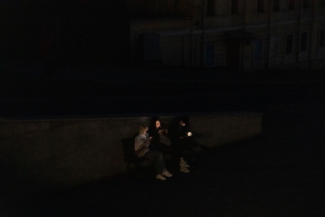 People sit on a bench as they check their smartphones in a street during a blackout following Russian attacks in Kharkiv, on April 8, 2024