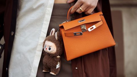 PARIS, FRANCE - MARCH 08: A guest wears brown coat, white blouse, orange Hermes bag with a bag charm brown Labubu monster, grey pants outside the Hermes fashion show during the Womenswear Fall/Winter 2025/2026 as part of Paris Fashion Week on March 08, 2025 in Paris, France. (Photo by Raimonda Kulikauskiene/Getty Images)