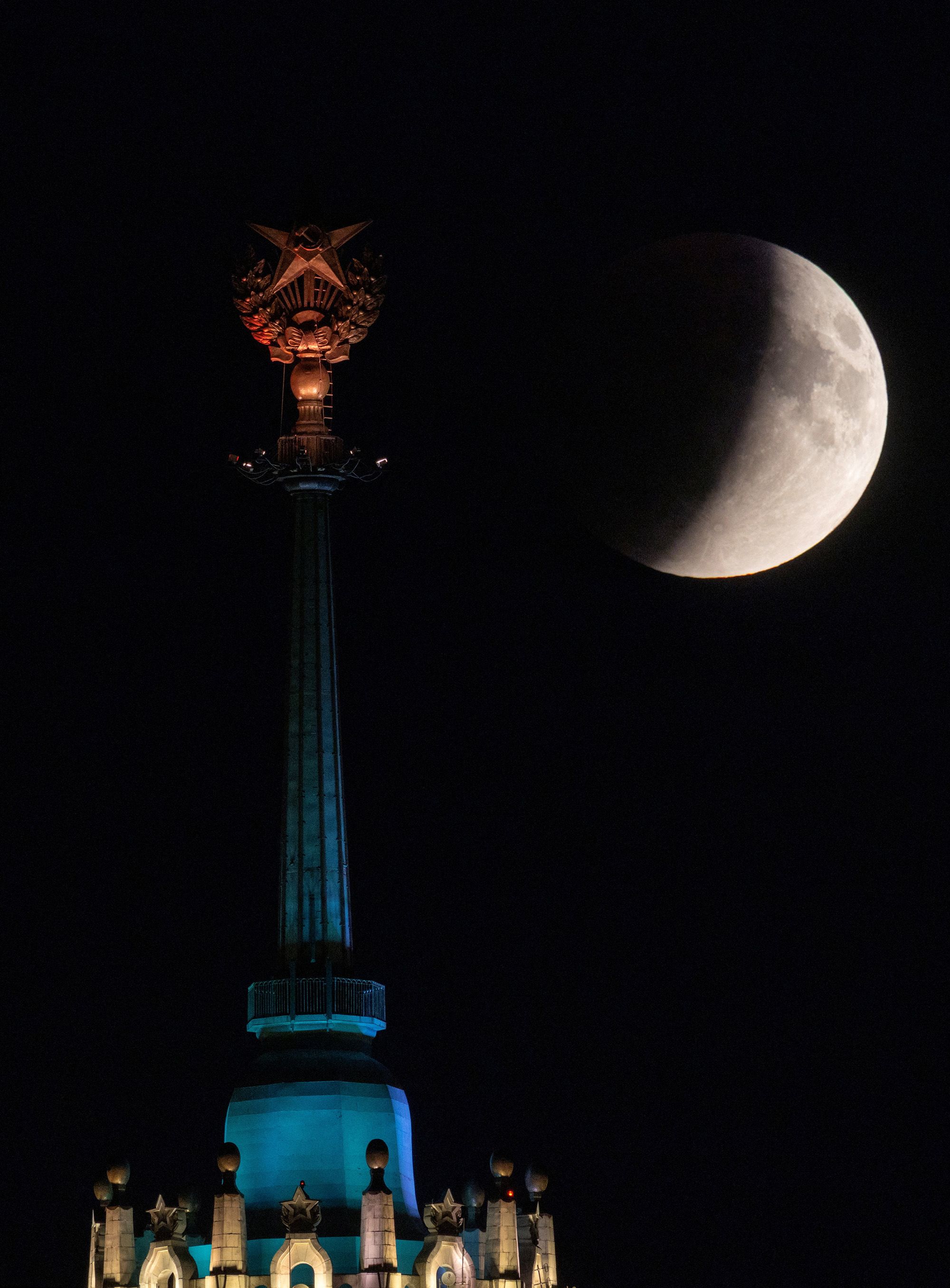 The eclipse rises behind a star on the top of the Kotelnicheskaya Embankment Building in Moscow.