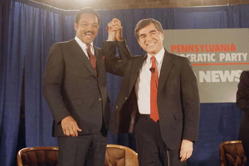 Jesse Jackson and Michael Dukakis raise their arms prior to a debate, at the University of Pennsylvania in April 1988.