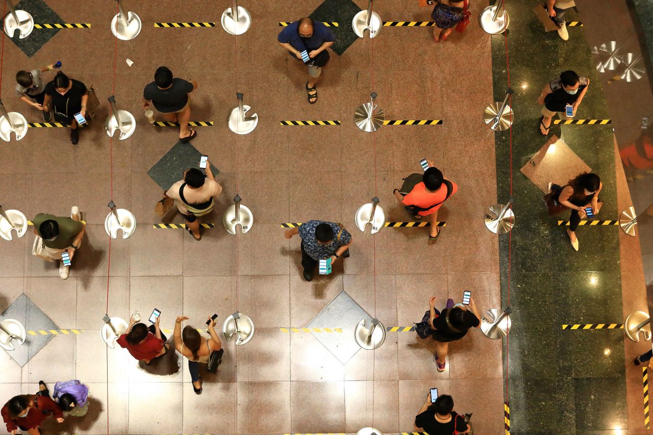 People wearing protective masks prepare their mobile phone for Safe Entry check-in as they queue to enter a shopping mall in Singapore, on Saturday, June 20