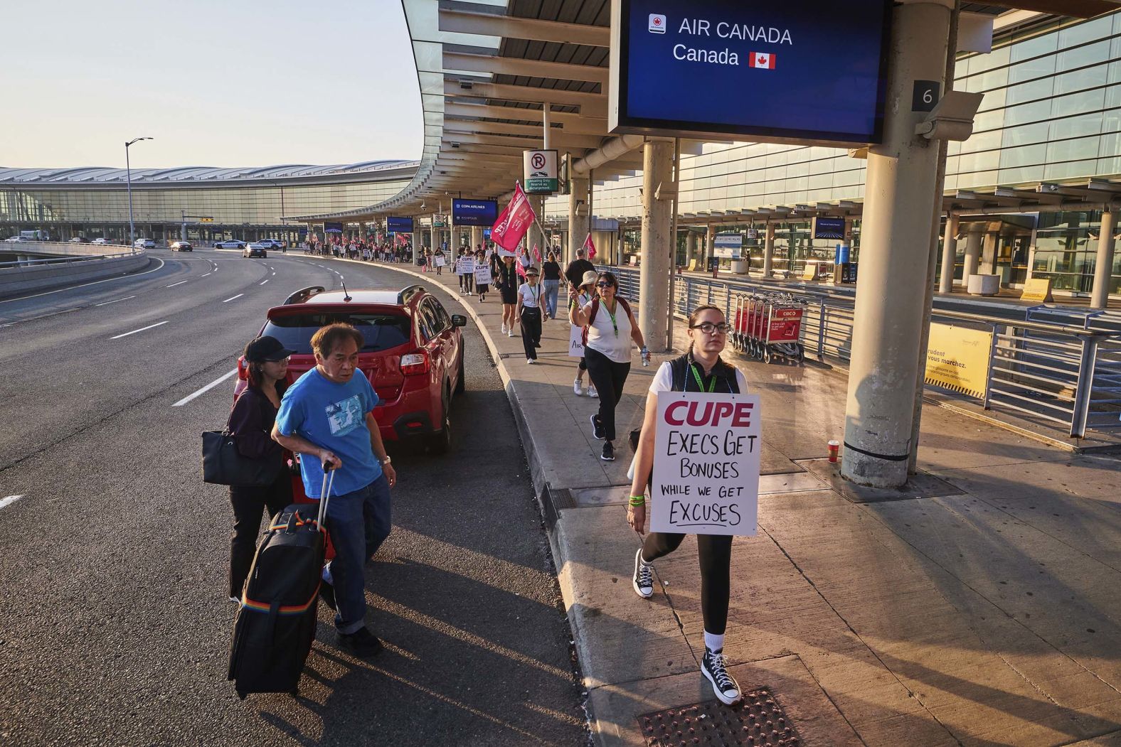 Travelers pass Air Canada flight attendants on strike at Pearson International Airport in Toronto on Saturday, August 16.