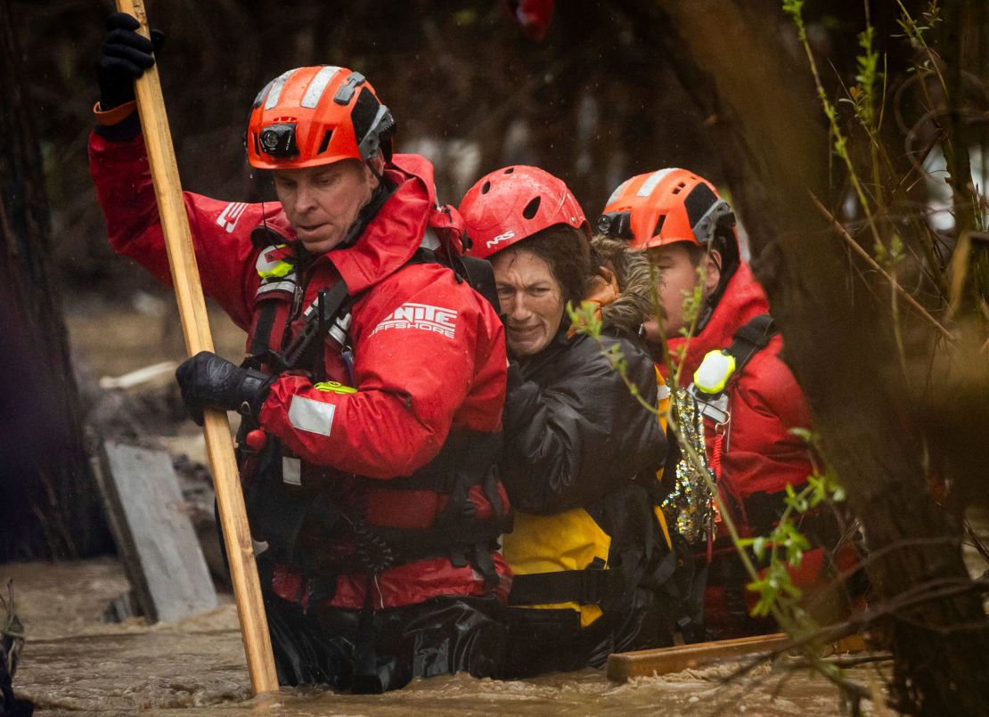 Firefighters rescue a woman from a homeless encampment that became surrounded by floodwater in the Santa Ana River on Monday in San Bernardino.