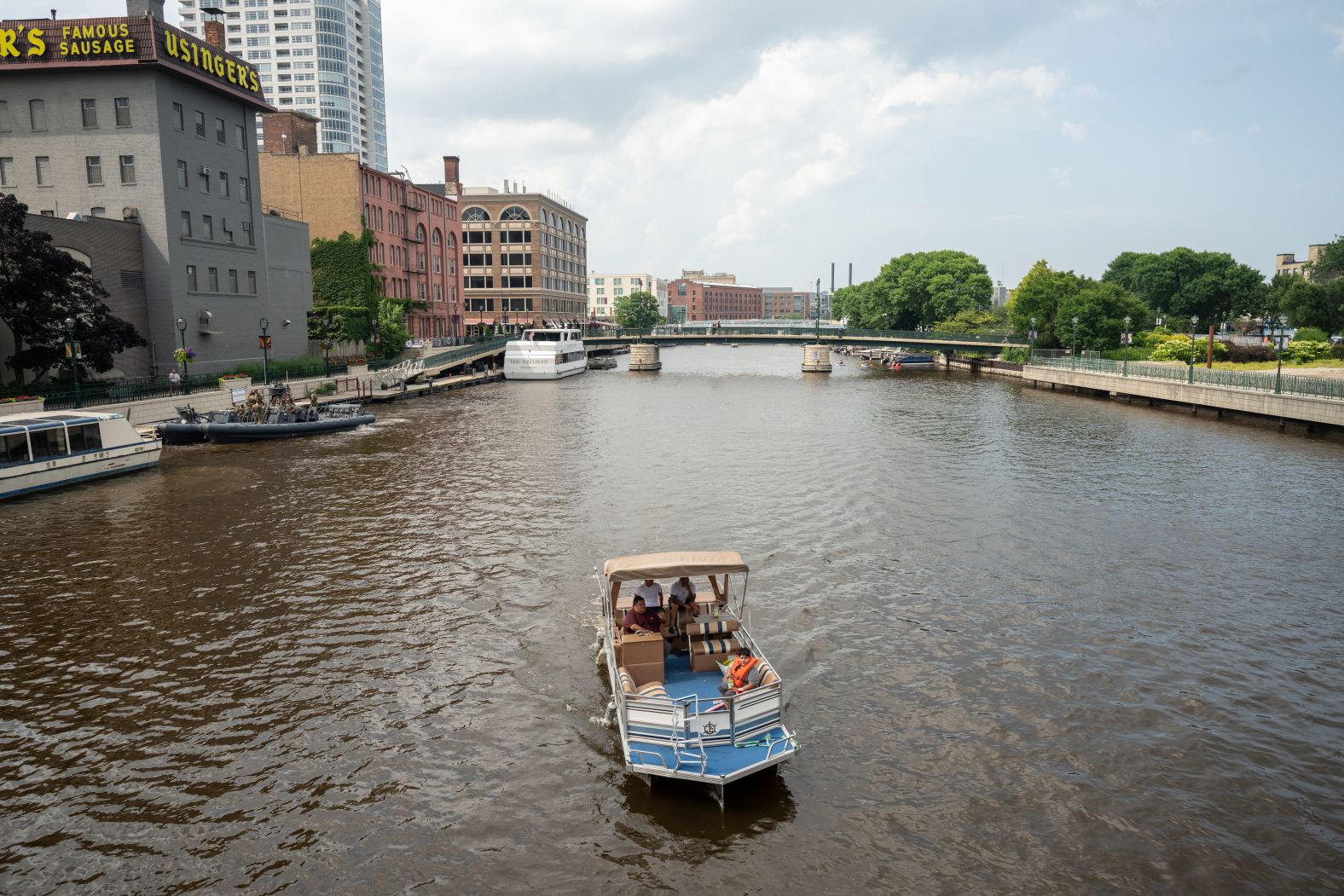 People ride a boat on the Milwaukee River on Saturday. Security personnel are seen on a boat in the distance.