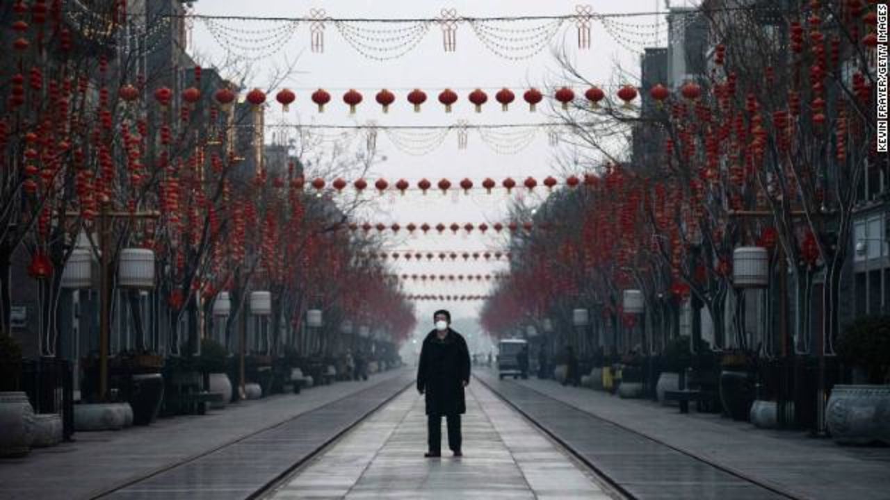 A Chinese man wears a protective mask as he walks in a nearly empty and shuttered commercial street in Beijing.