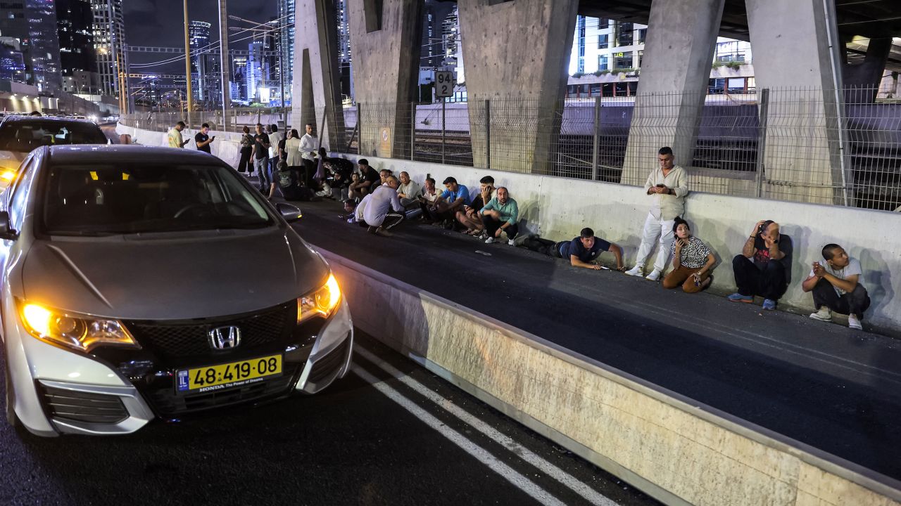 People take cover behind vehicles under a bridge along in Tel Aviv.