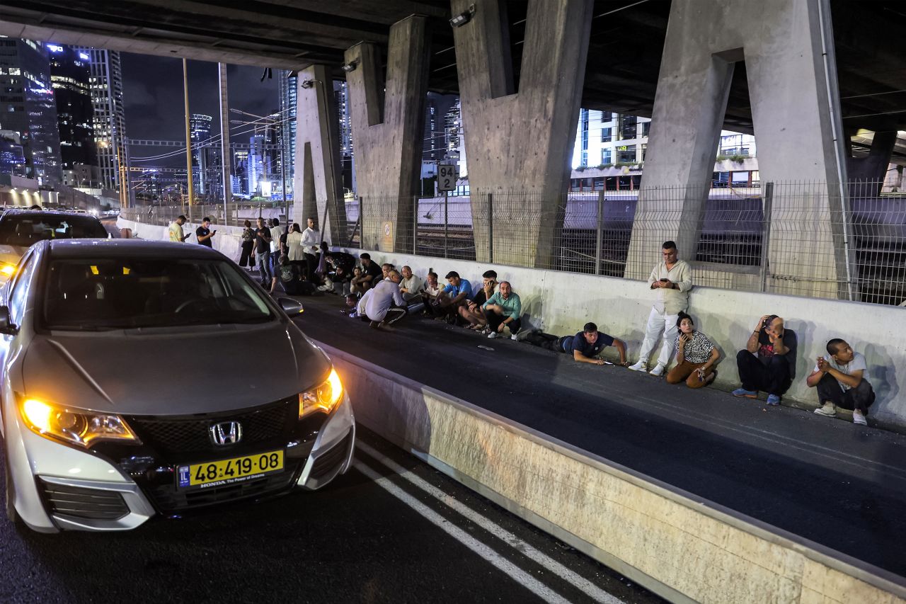 People take cover behind vehicles under a bridge along in Tel Aviv.