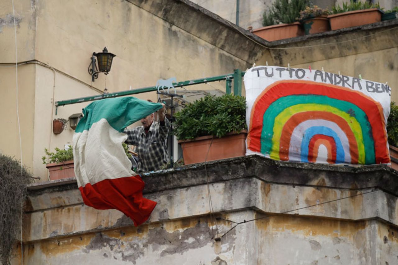 A man unfolds an Italian flag as he stands next to a banner reading everything will be alright, at the Garbatella neighborhood, in Rome, Saturday, March 14. 