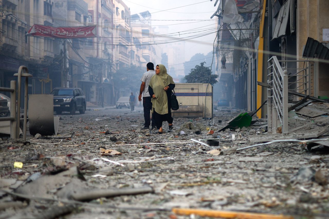 A Palestinian woman looks on as she walks on a debris-strewn street near the Watan Tower, which was destroyed in?Israeli strikes, in Gaza City on October 8, 2023.