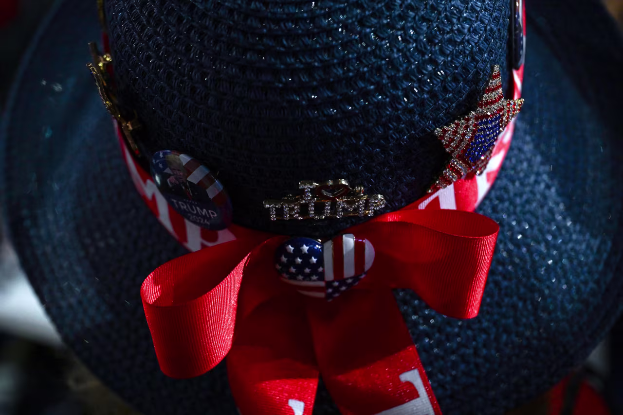 A woman wears a hat with Trump's name on it.