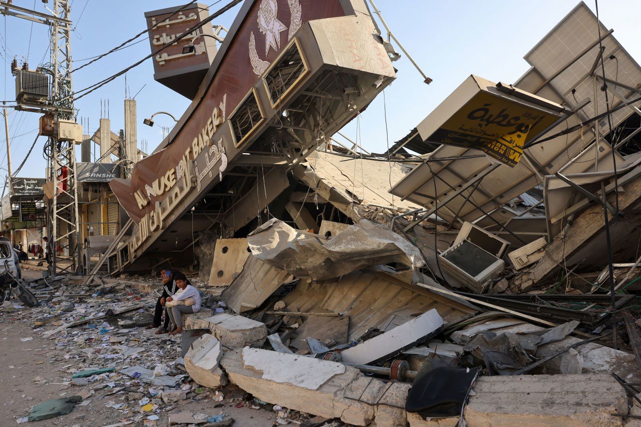 A Palestinian man and his son sit holding a bag of bread outside a destroyed bakery at the Nuseirat refugee camp in the central Gaza on November 4. 