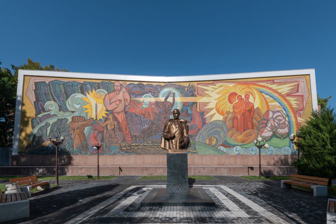 A statue of poet Taras Shevchenko stands before a Soviet-era mosaic mural in Tashkent.