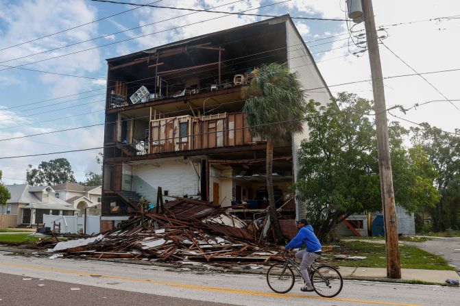 A person rides a bicycle past a damaged building in the Palmetto Beach neighborhood of Tampa on Thursday.