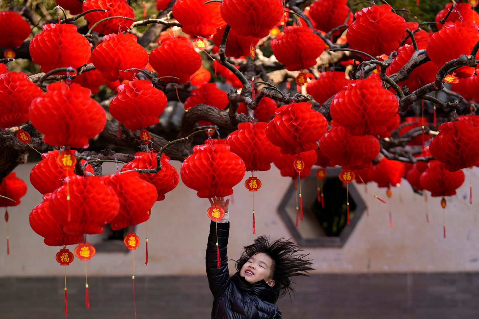 A child jumps to touch red lanterns hung on trees at the Ditan Park in Beijing on Wednesday.