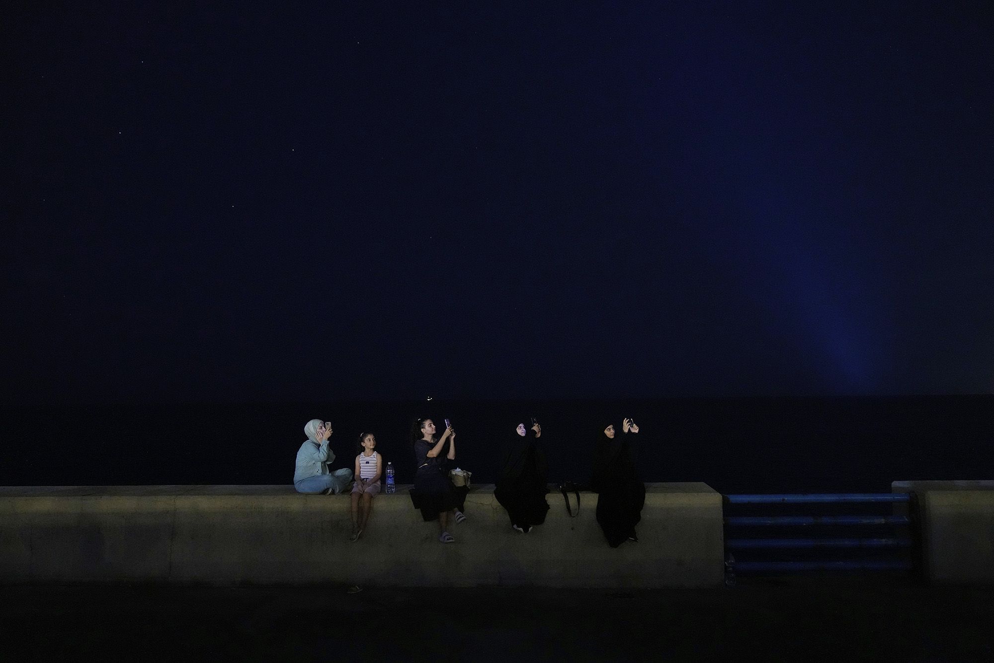 People take pictures of the lunar eclipse along a  Mediterranean waterfront promenade in Beirut on Sunday.