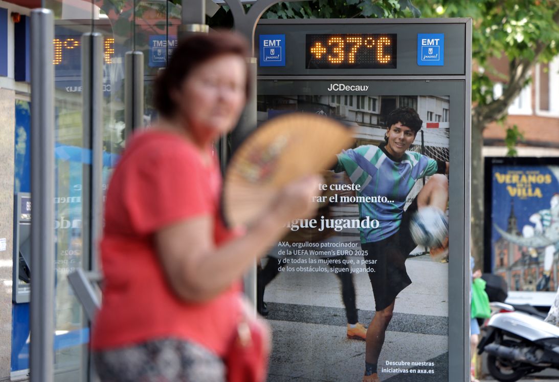 A woman cools herself off using a fan at a bus stop showing a temperature of 37 degrees Celsius during a heatwave in Madrid, on July 1, 2025.