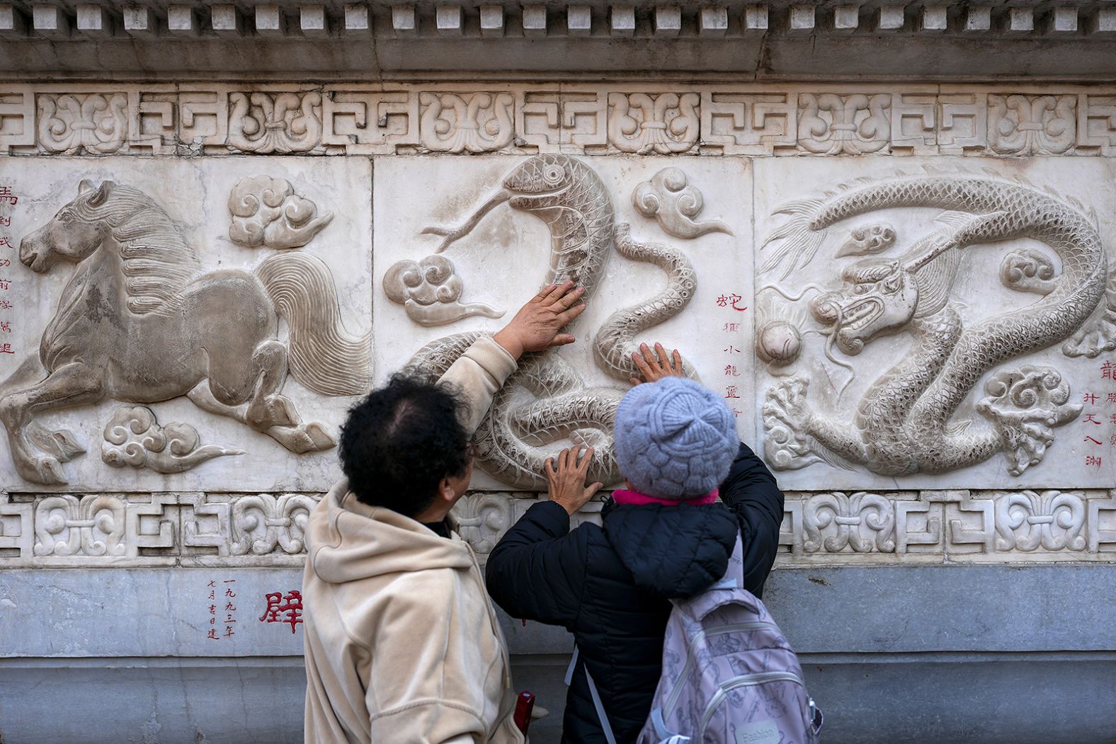 Women touch the snake figure on a stone wall at Baiyun Taoist Temple in Beijing on Wednesday, January 22. The Year of the Snake starts on January 29.