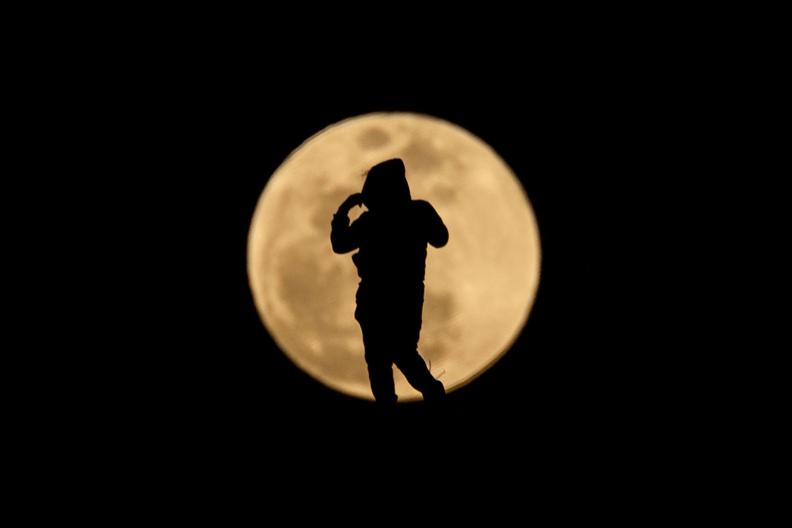 A person is silhouetted against the full moon, as it rises over Los Angeles ahead of the lunar eclipse.