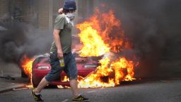 A masked man walks past a burning car outside a Carhartt store in Hackney on August 8, 2011 in London, England.