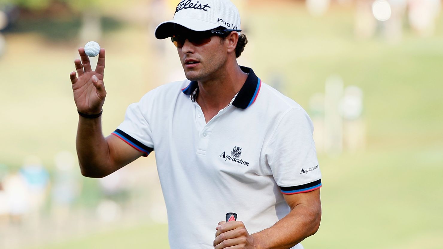 Adam Scott waves to the gallery after a birdie putt on the 18th green puts him top of the leaderboard.