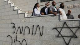 Israeli rabbi Menachem Froman condemns an arson attack by settlers while standing on September 6, 2011 above Hebrew graffiti on the outside wall of a mosque .