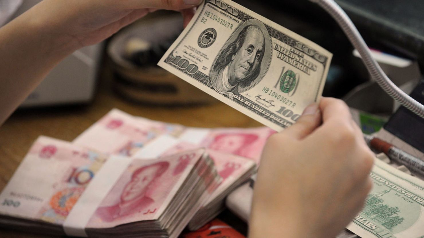 A Chinese bank worker checks a $100 bill together with stacks of 100 yuan notes at a bank in Hefei, east China, on September 30, 2010. 