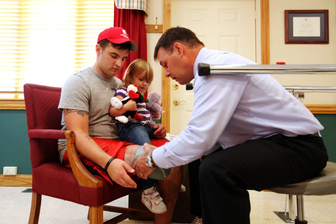 Roger Howard helps Matthew Hayes, with his daughter, get fitted for a new prosthetic leg.