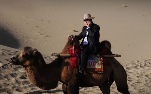 A Chinese tourist talks on his phone while riding a camel through the sand dunes in China's northwest Gansu province on September 27, 2008. Low-cost cell phone towers allows mobile coverage in ever more remote locations.