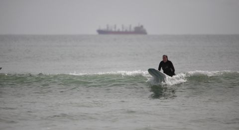 A surfer catches a wave with the main cargo route in the background near the port of Tauranga on October 8. 