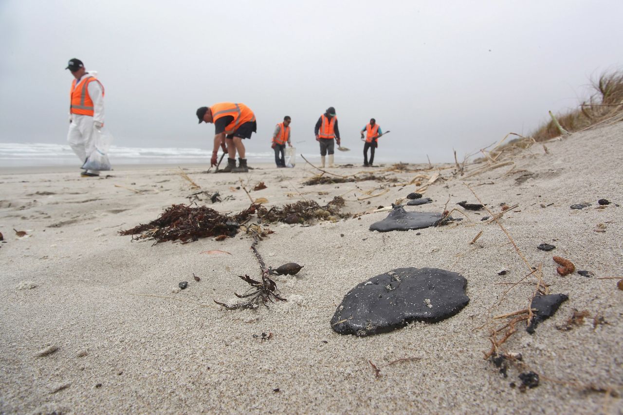 Volunteers collect oil clumps washed up on the Mount Maunganui shore on October 11 in Tauranga.