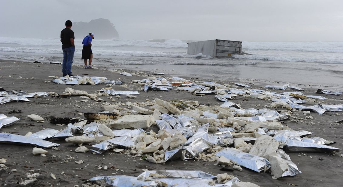 Local residents come to look at a washed-up container and litter on the beach on October 13.