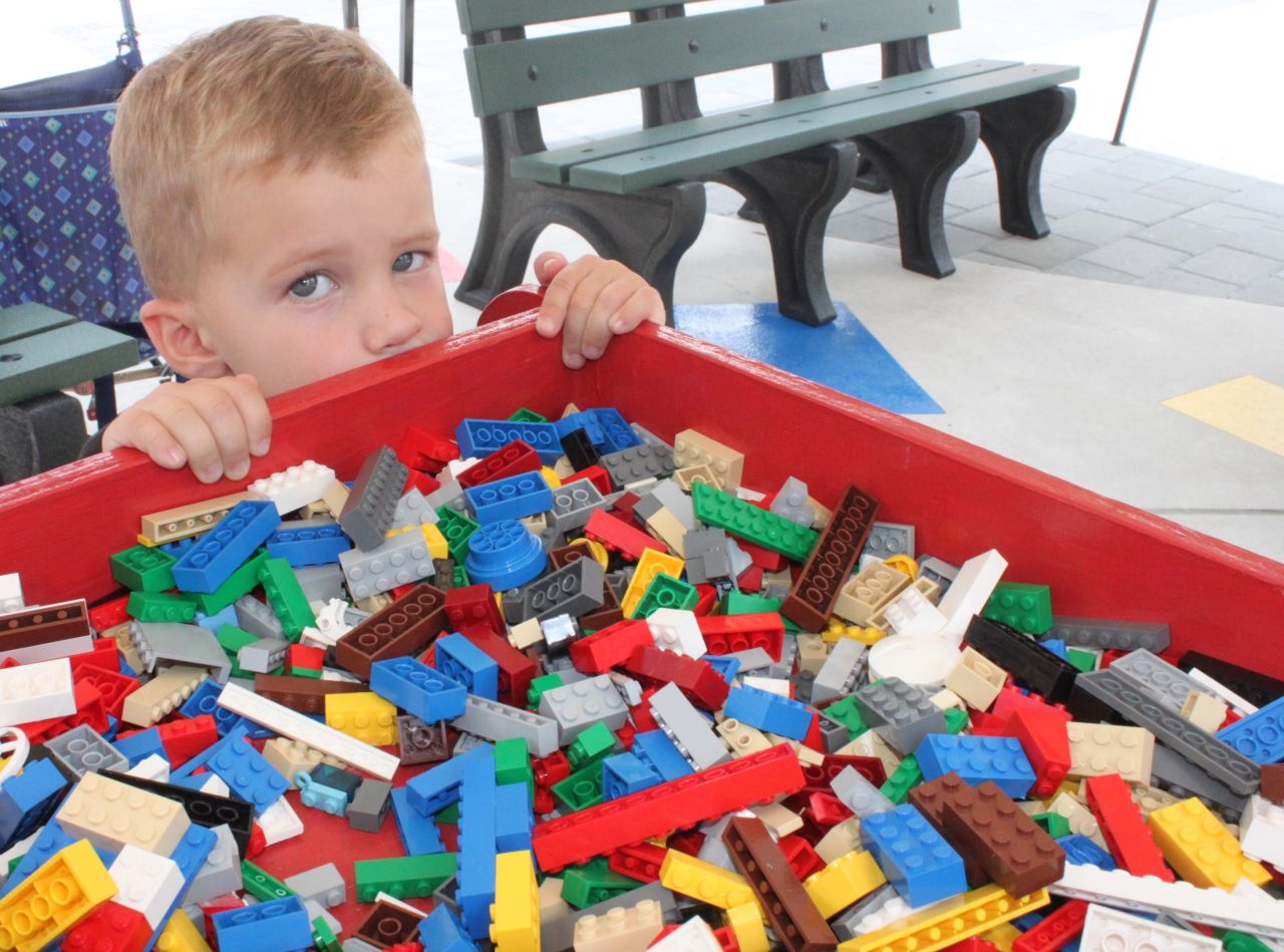 Three-year-old Cole Herbet crouches behind a big Lego bin while his grandparents buy annual passes to the new park.