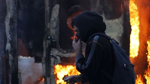 A protester covers his face and holds a stone as he walks in front of a burning in Athens .