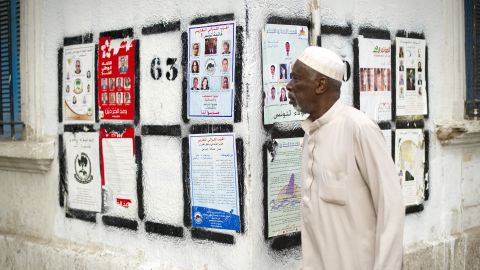 	A Tunisian man walks past a wall covered with posters of political candidates on Bourguiba Avenue in Tunis.