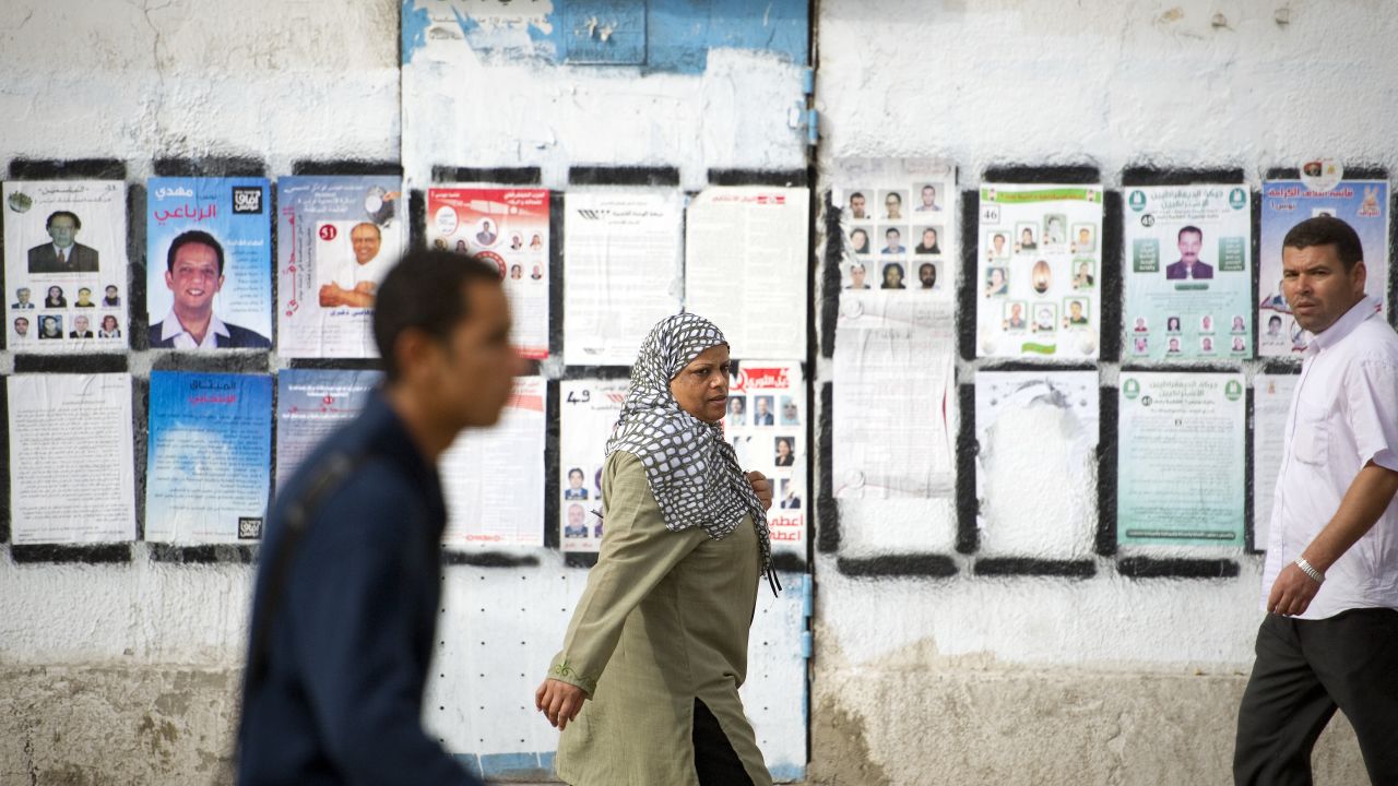 Tunisian people walk past a wall covered with posters of political candidates in Tunis two days before a historic election.