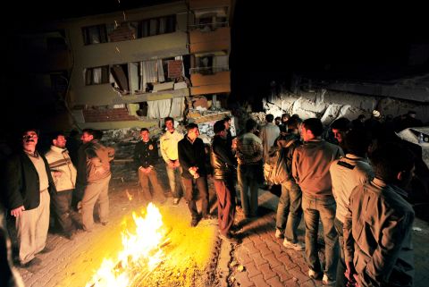 Ercis residents gather around a fire in the street and survey the destruction of the surrounding city on Sunday.