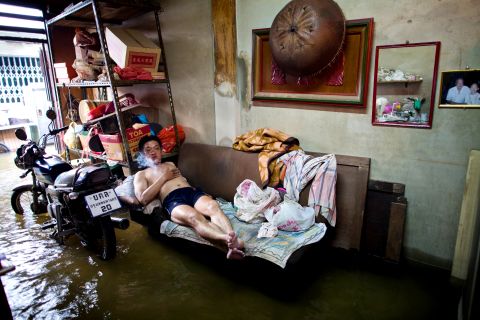 A man lies on a couch Wednesday in his flooded Bangkok home. Gov. Sukhumbhand Paripatra says that despite the risk, it is difficult to persuade people to leave their homes.