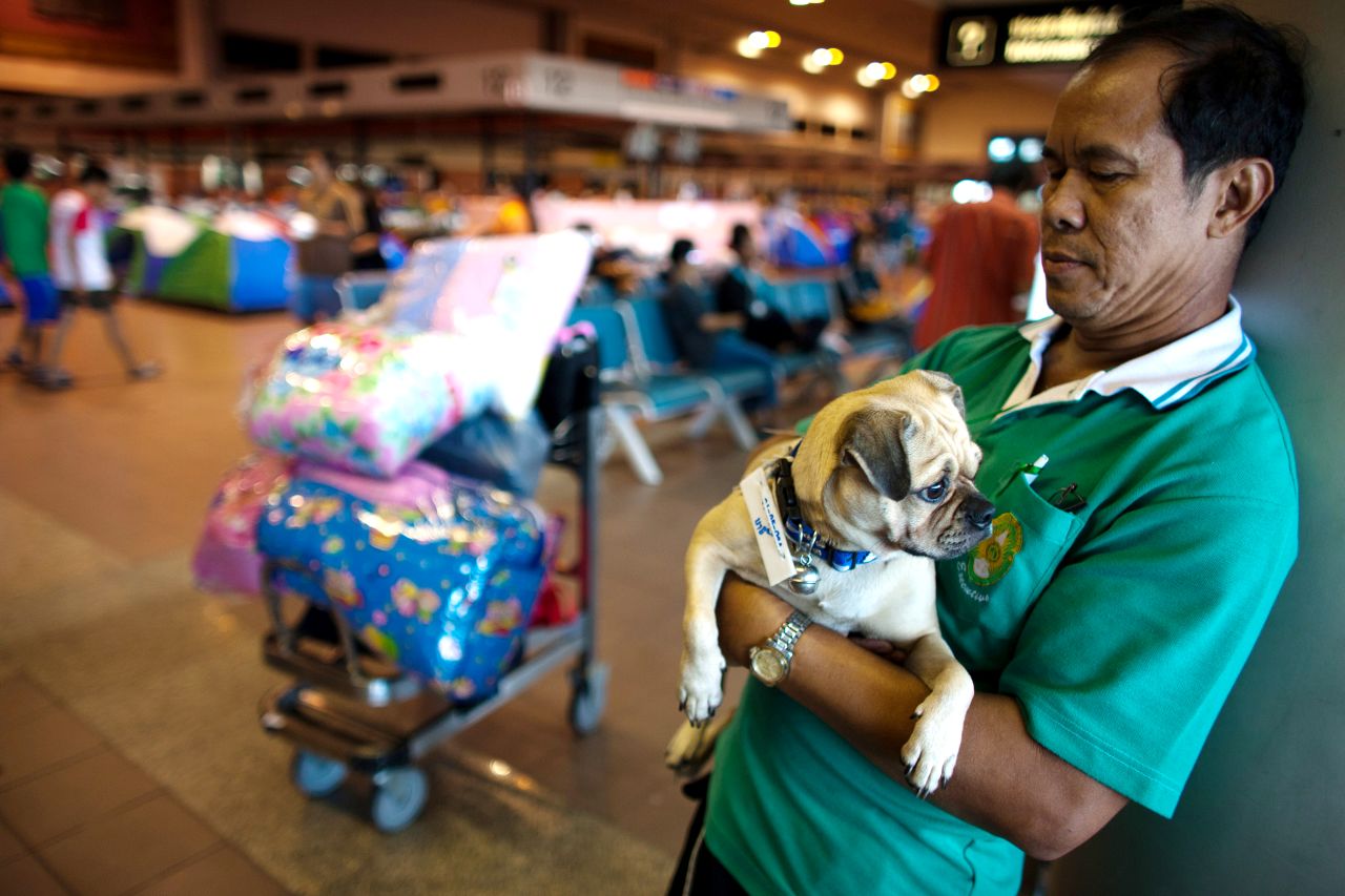 A man holds his dog and stands by his belongings at the Don Muang airport. He's waiting to be transferred to a new evacuation center.