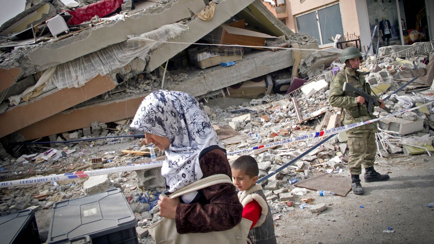  A woman and child walk past a collapsed building, as a soldier stands guard after the earthquake. 
