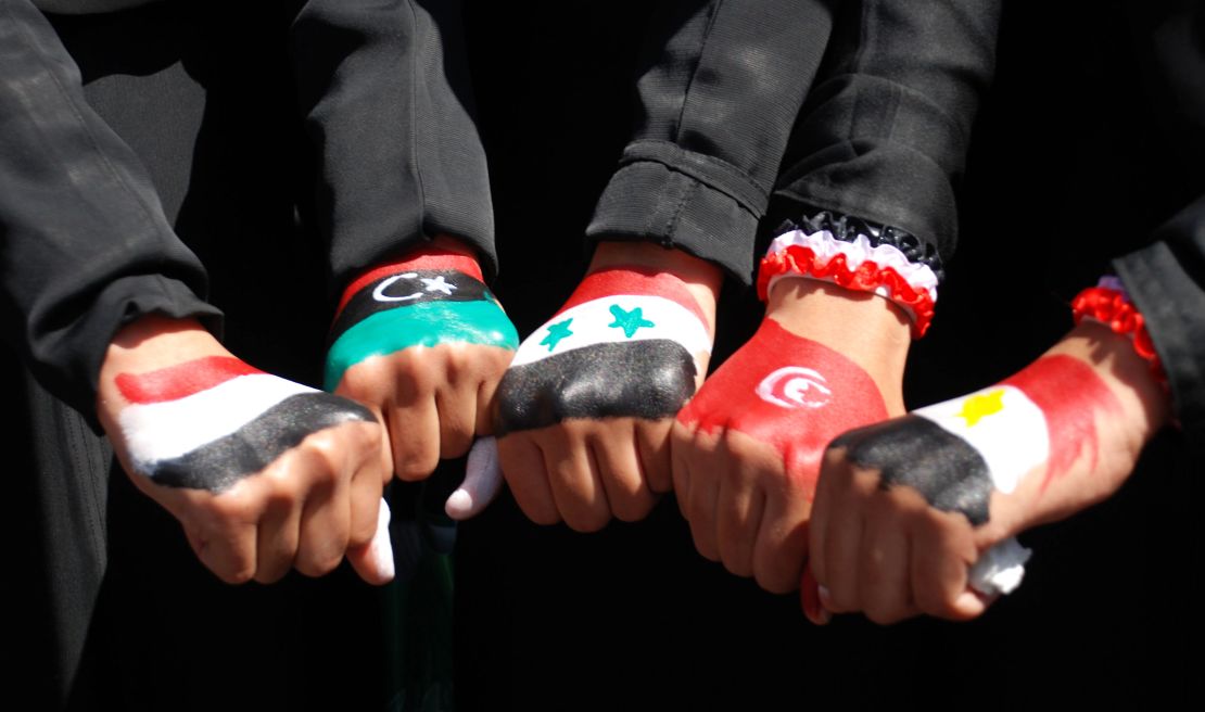 Yemenis women show off their fists painted in the colors of five Arab national flags