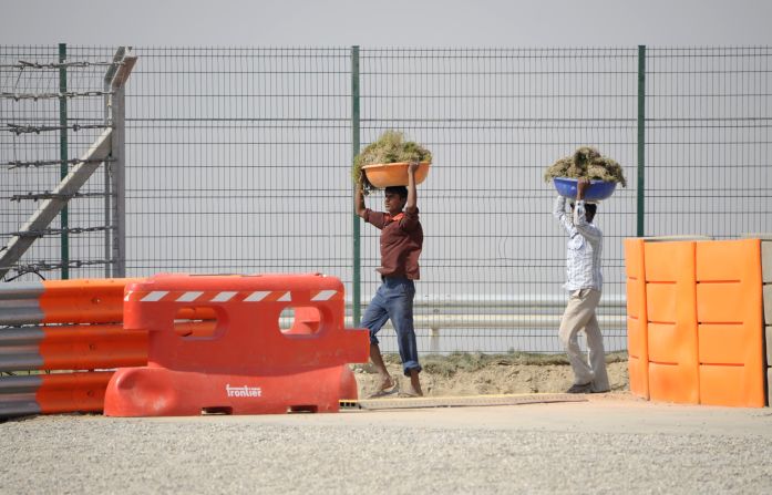 Workers carry grass as they make final preparations the day before opening practice.