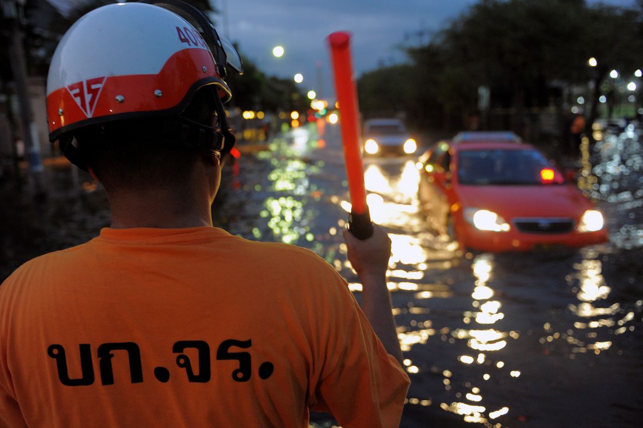 A Thai police officer directs traffic as cars pass through flooded streets on Friday. Residents have begun leaving Bangkok to escape the rising waters. 