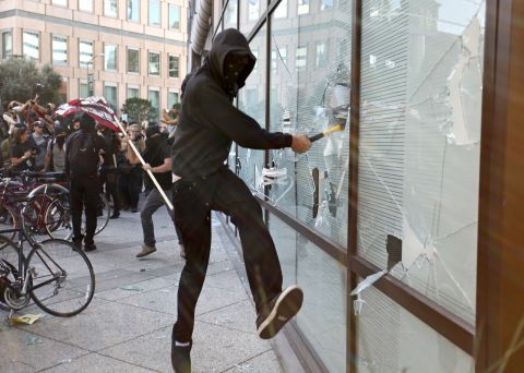 A masked protester smashes a window at a Wells Fargo bank during the citywide general strike Wednesday. Police said a small group vandalized some Oakland businesses, including banks and a grocery store.