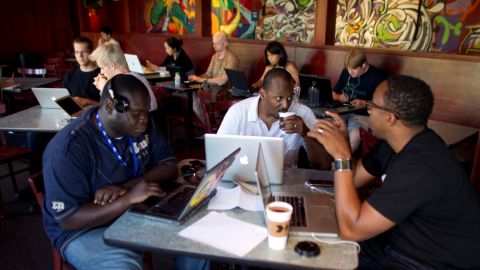 NewMe co-founder Wayne Sutton, center, works on his laptop at a coffee shop with fellow entrepeneurs.