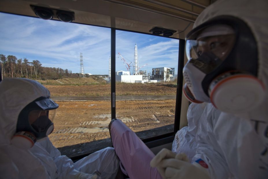 People wearing protective suits and masks ride on a bus past the crippled Fukushima Daiichi nuclear power station in Okuma, Japan, on Saturday, November 12 2012.  Journalists got their first ground-level glance  around the stricken facility, eying shells of reactor buildings, tons of contaminated water, and workers still scurrying to mitigate damage from a crisis that began eight months ago.