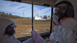 People wearing protective suits and masks ride on a bus past the crippled Fukushima Daiichi nuclear power station in Okuma, Japan, on Saturday, November 12 2012.  Journalists got their first ground-level glance  around the stricken facility, eying shells of reactor buildings, tons of contaminated water, and workers still scurrying to mitigate damage from a crisis that began eight months ago.