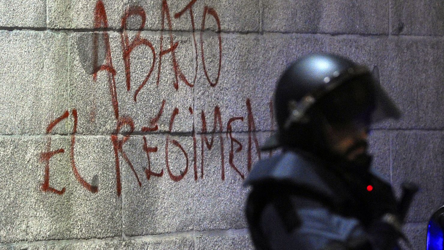 Graffiti says "Down with the regime" on Spain's parliament building near a riot officer during a protest before elections this month.
